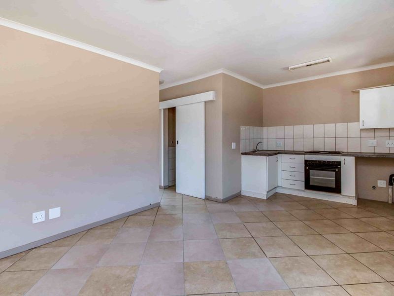 Open plan living area featuring a compact kitchen with built-in oven, hob, and tiled flooring throughout.