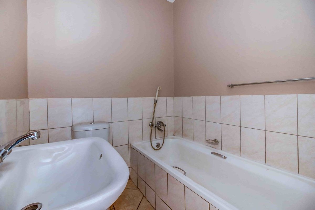 A functional bathroom featuring a standard bathtub with a handheld shower mixer, a pedestal basin, and neutral ceramic wall tiling.