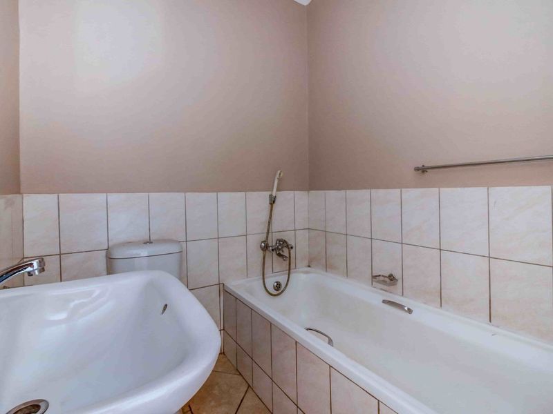 A functional bathroom featuring a standard bathtub with a handheld shower mixer, a pedestal basin, and neutral ceramic wall tiling.