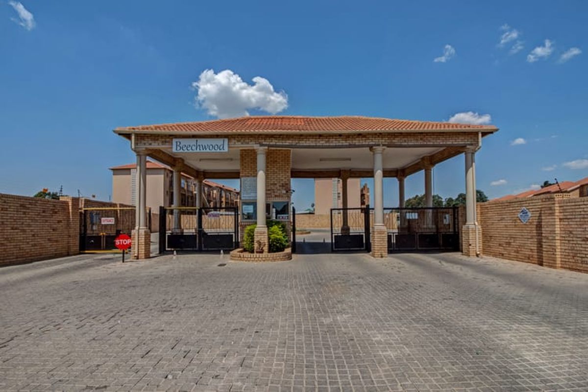 The main entrance to the Beechwood apartment complex, featuring a secure gated access point, guard house, and brick perimeter walling.