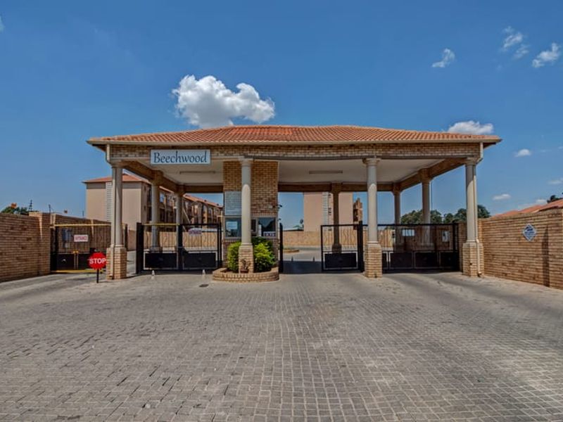 The main entrance to the Beechwood apartment complex, featuring a secure gated access point, guard house, and brick perimeter walling.