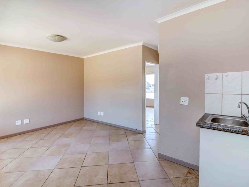 An empty open-plan living area featuring tiled flooring and a compact kitchen corner with a sink and tiled splashback.