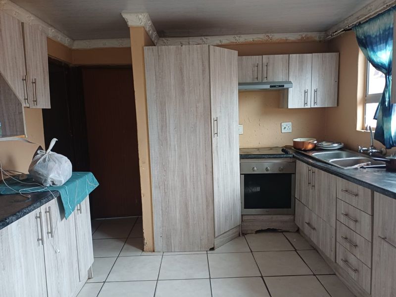 A functional kitchen featuring light wood-grain cabinetry, built-in oven and hob, extractor fan, double sink, and tiled flooring.