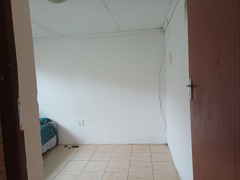 A basic bedroom featuring tiled flooring, plain white walls, and a standard wooden door, requiring some cosmetic updates and repairs.