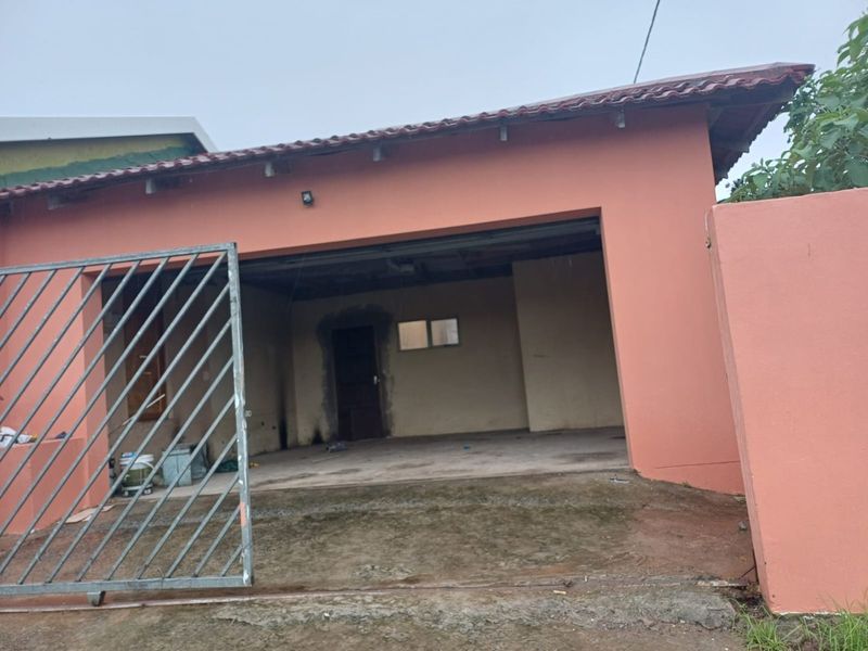 A view of the property's garage entrance featuring a metal gate, concrete driveway, and unfinished plasterwork around the doorway.