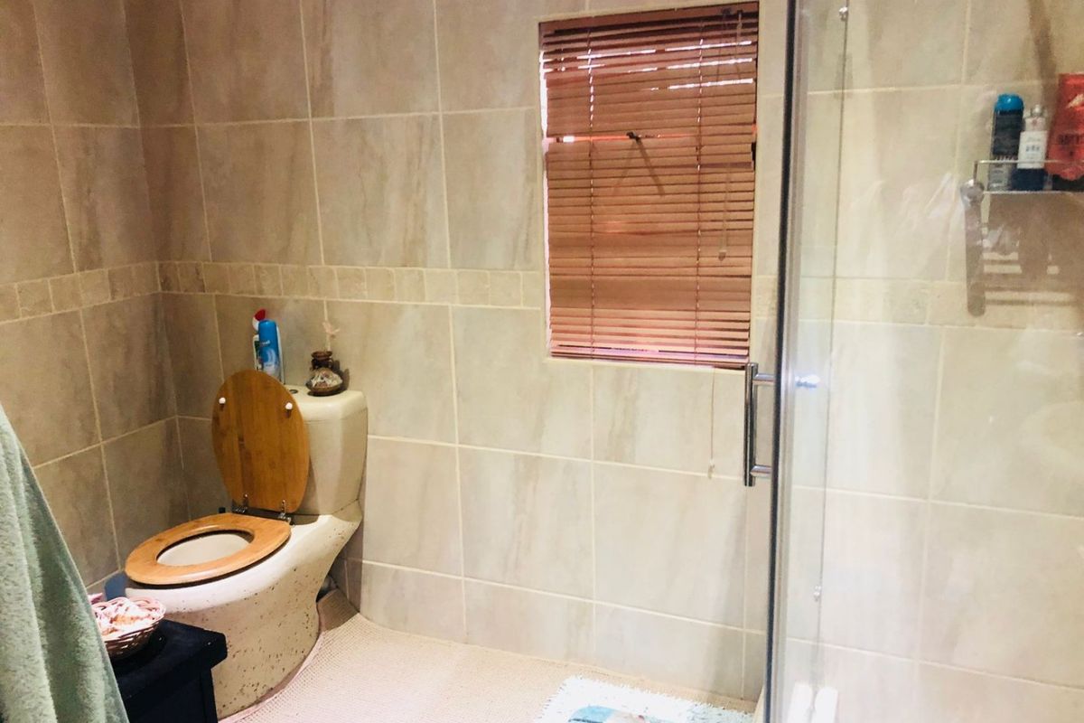 A functional bathroom featuring floor-to-ceiling wall tiles, a glass-enclosed shower, and a standard toilet.