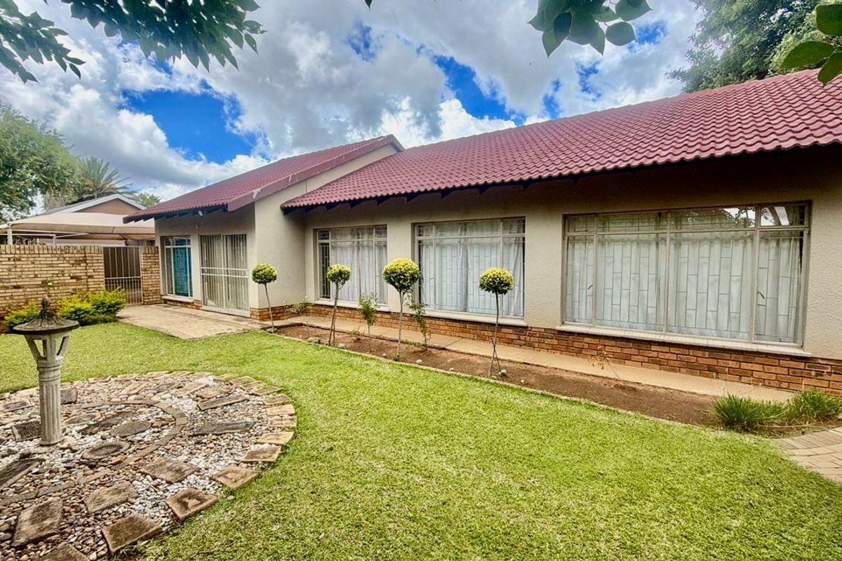 A well-maintained rear exterior view of the house featuring a tiled roof, brick facade, paved patio area, and a landscaped garden.