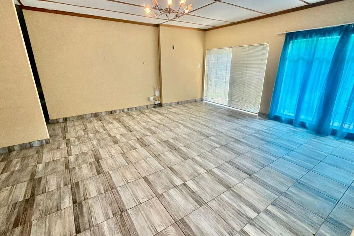 An empty living room featuring wood-look tiled flooring, sliding glass doors with blinds, and a drop ceiling with a central light fixture.