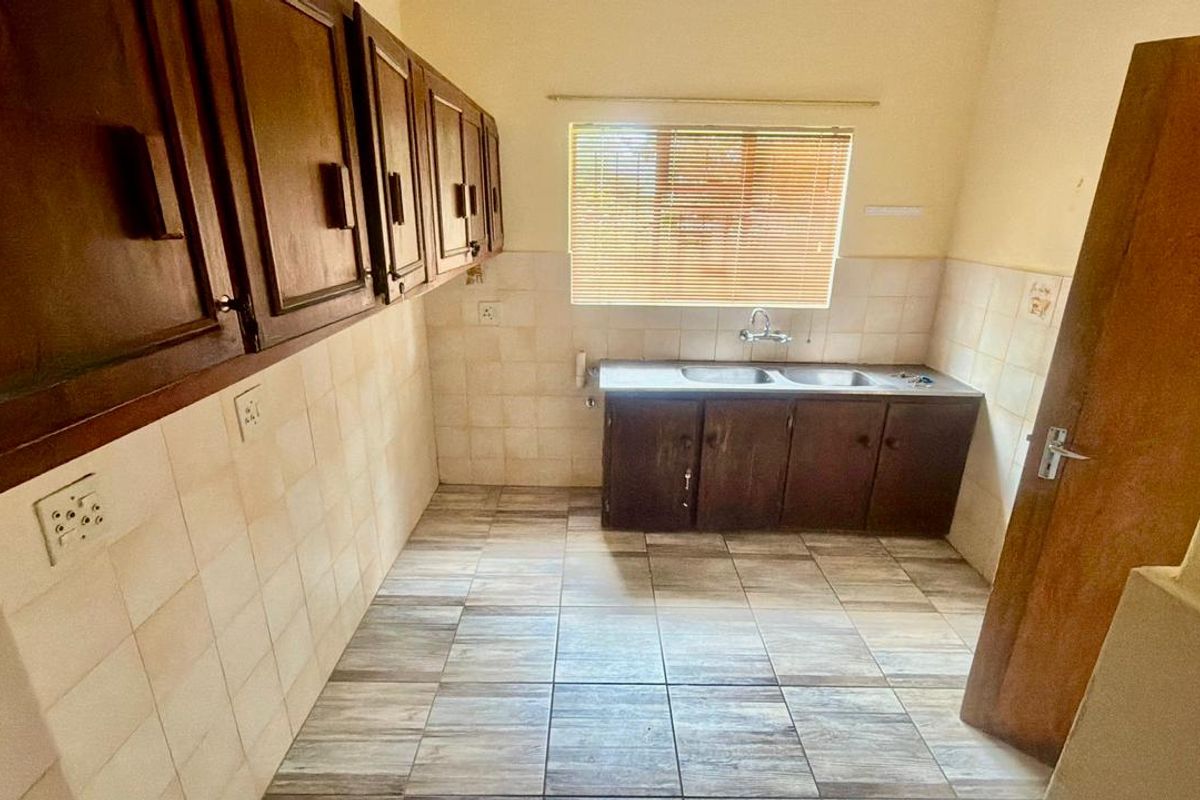 A functional kitchen space featuring built-in wooden cabinetry, a double stainless steel sink, tiled splashbacks, and tiled flooring.