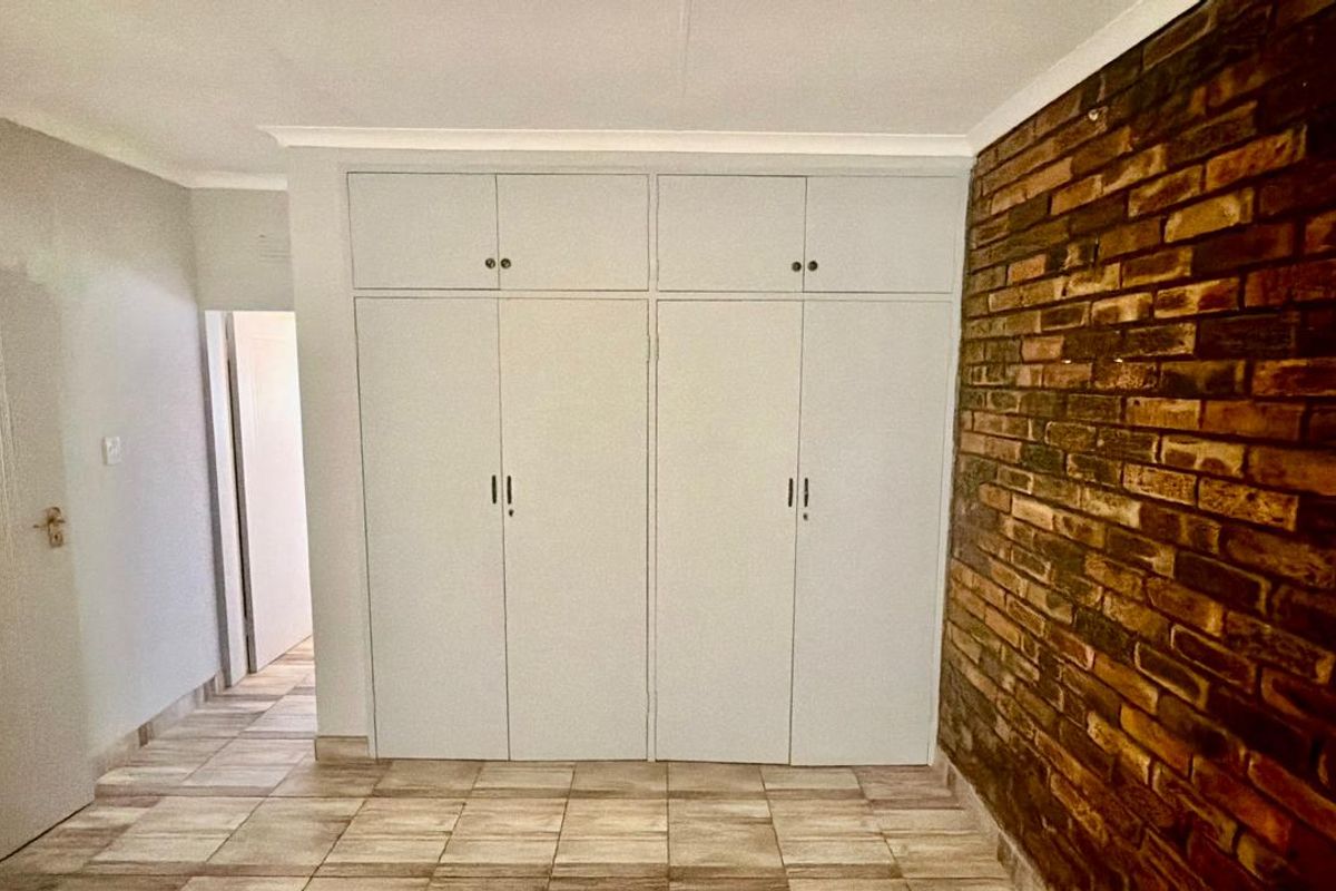 A bedroom featuring built-in cupboards, a rustic exposed brick feature wall, and tiled flooring.