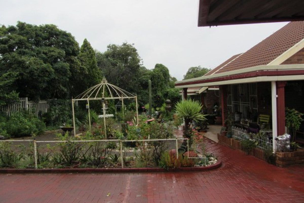 A rear exterior view featuring a covered patio area, brick paving, and a metal gazebo set within a landscaped garden.
