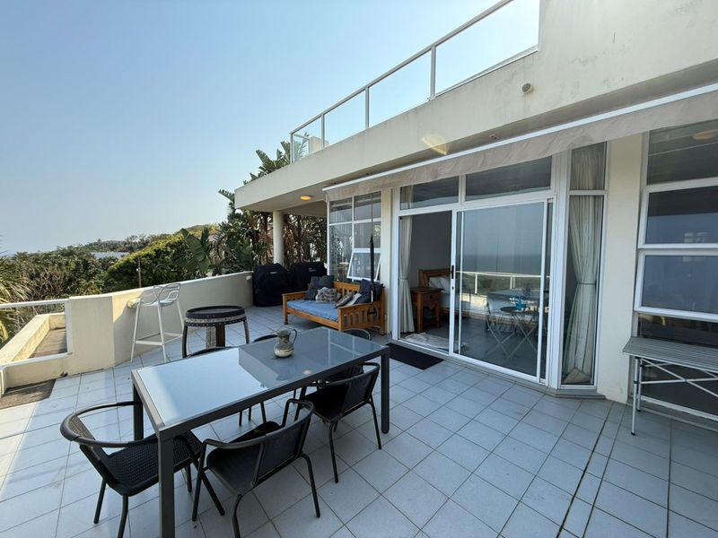 Spacious outdoor balcony featuring tiled flooring, a glass balustrade, and a retractable awning, providing seamless access to the interior living space.