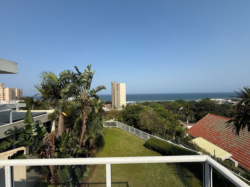 Elevated view overlooking a landscaped garden, surrounding neighborhood, and the ocean horizon from a balcony.