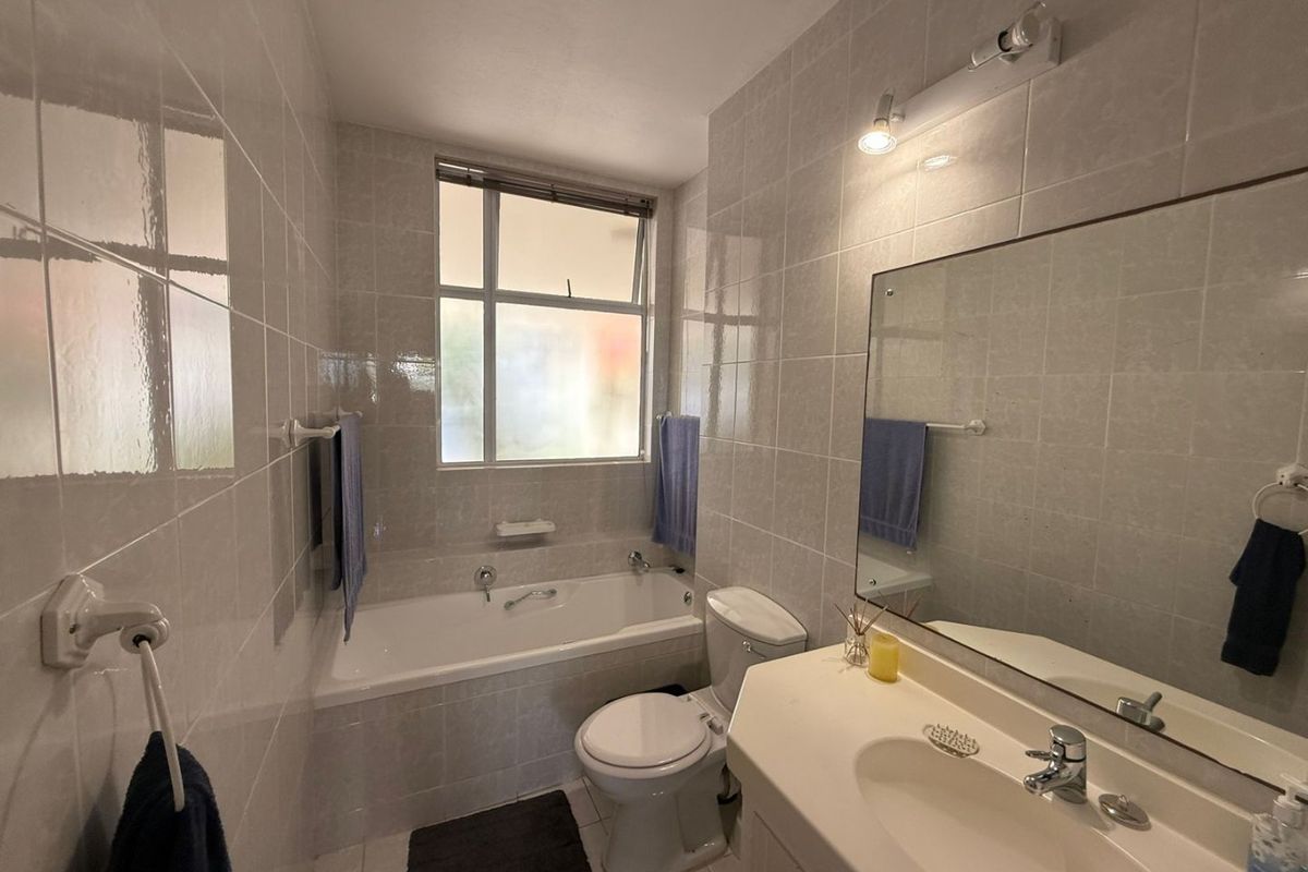 A functional bathroom featuring a built-in bathtub, wall-mounted vanity with basin, and full-height ceramic wall tiling.