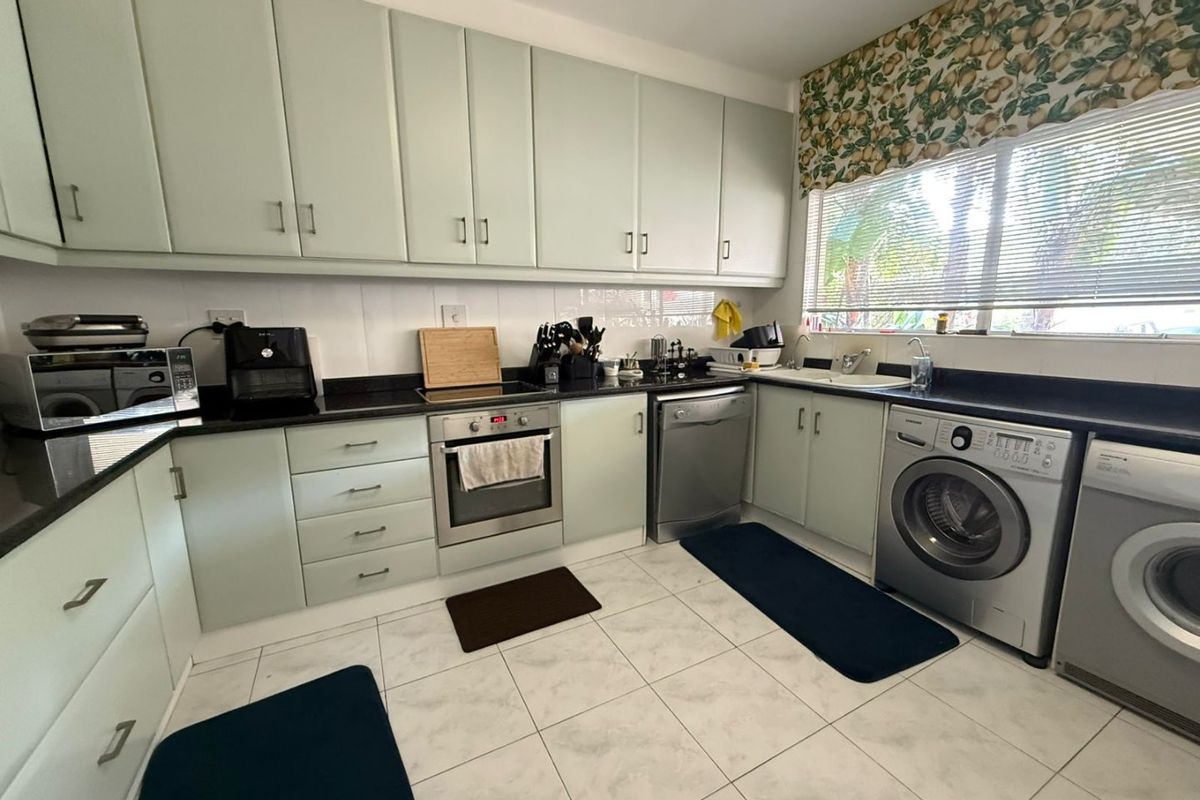 A functional kitchen featuring light-toned cabinetry, dark stone countertops, integrated oven, and tiled flooring with space for laundry appliances.