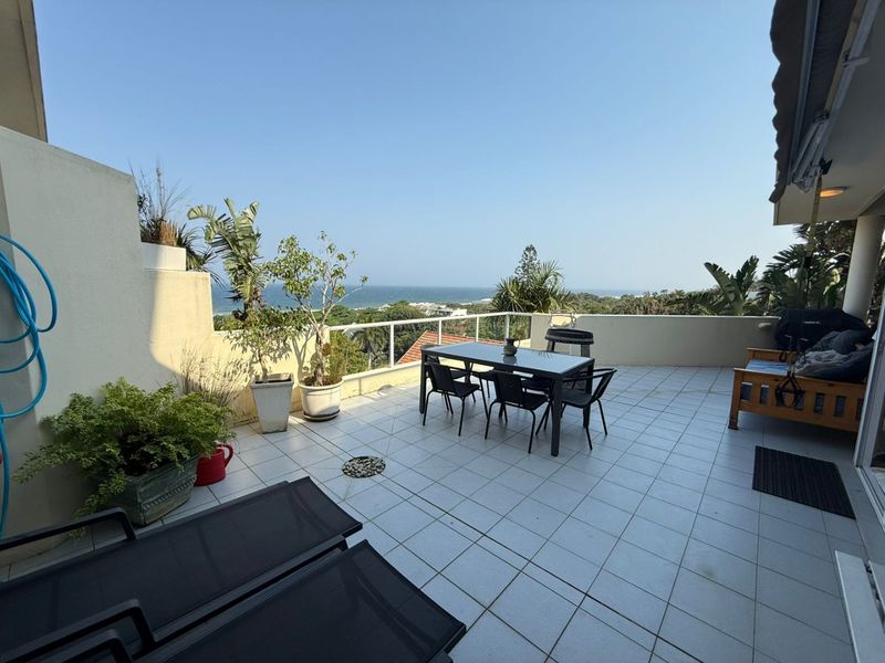 Spacious outdoor balcony featuring tiled flooring, a glass balustrade, and a retractable awning, offering expansive coastal and ocean views.