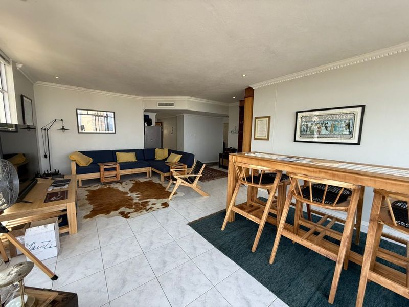 An open-plan living and dining area featuring tiled flooring, crown molding, and recessed lighting, providing a versatile space for relaxation and entertaining.