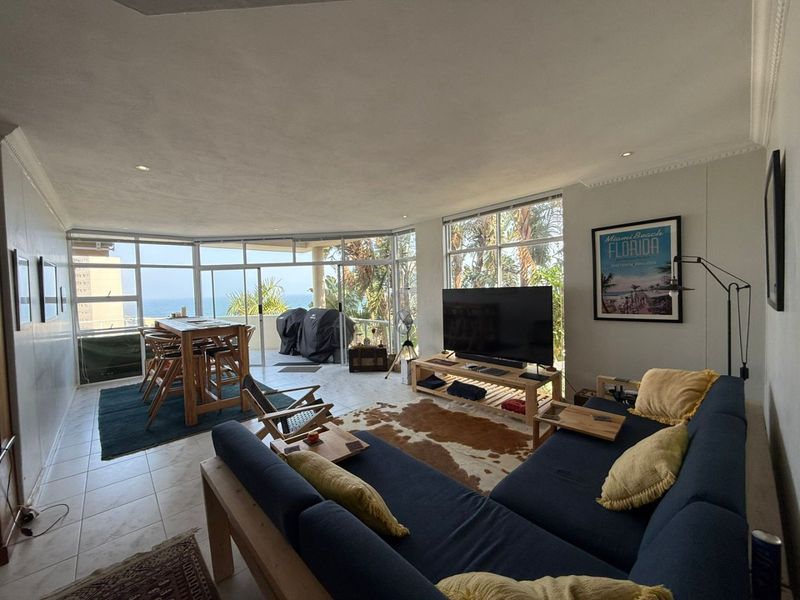 Spacious open-plan living area featuring tiled floors, recessed lighting, and expansive glass doors leading to a balcony with ocean views.