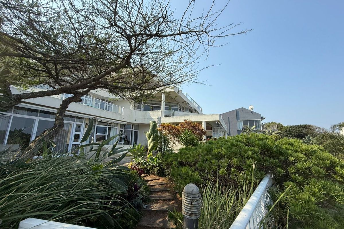 Rear view of the apartment building featuring a landscaped garden, paved pathway, and multiple levels of balconies with sliding glass doors.