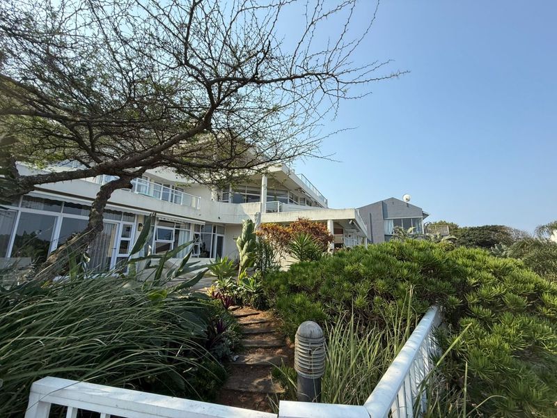 Rear view of the apartment building featuring a landscaped garden, paved pathway, and multiple levels of balconies with sliding glass doors.