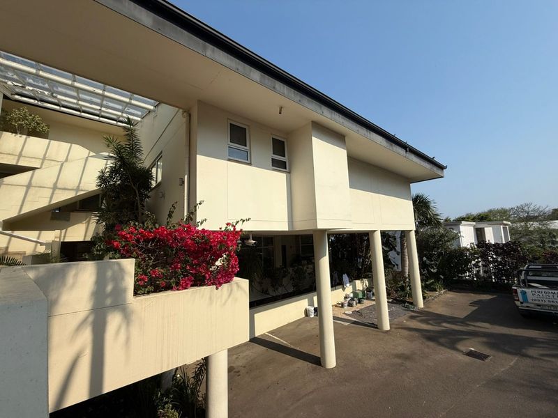 Exterior view of an apartment building featuring concrete support columns, a paved driveway, and an elevated balcony area.