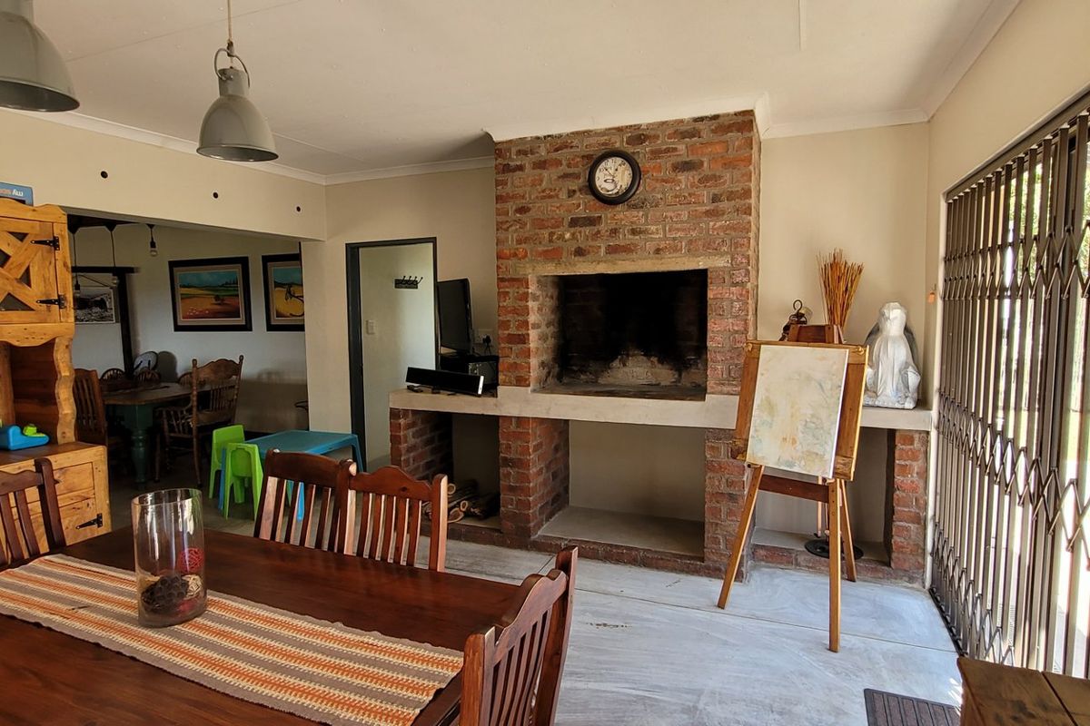 Spacious living area featuring a prominent brick fireplace with built-in braai, tiled flooring, and direct access to the exterior through a security gate.