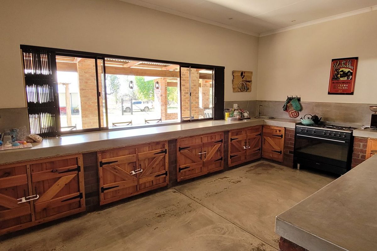 Rustic farmhouse kitchen featuring custom wooden cabinetry, durable concrete countertops, and a large sliding window overlooking the outdoor area.