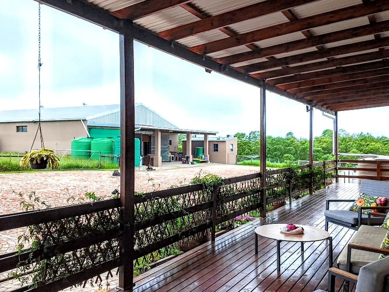 A spacious covered wooden deck overlooking a paved farm courtyard with large water storage tanks and outbuildings in the background.