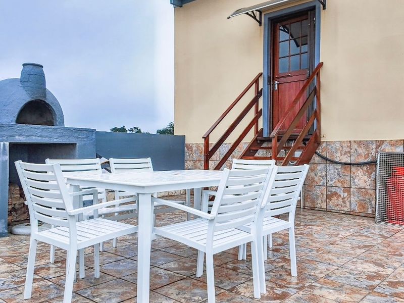Outdoor patio area featuring a built-in masonry braai, tiled flooring, and direct access to the building via a wooden staircase.