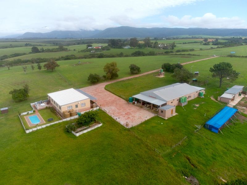 Aerial view of a farm property featuring a main residence with a swimming pool, a large workshop or barn, and extensive surrounding pasture land.