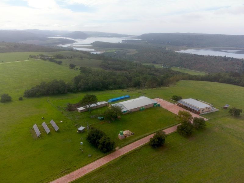 Aerial view of a farm property featuring multiple outbuildings, solar panel arrays, water storage tanks, and expansive surrounding landscape with scenic water views.