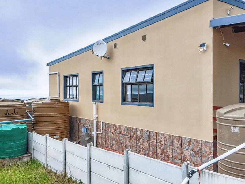 Rear exterior view of the farm property featuring multiple water storage tanks, security cameras, and tiled lower wall cladding.