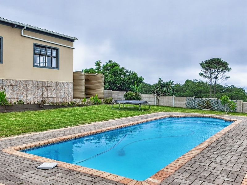A well-maintained outdoor pool area featuring a paved surround, manicured lawn, and water storage tanks set against a rural landscape.