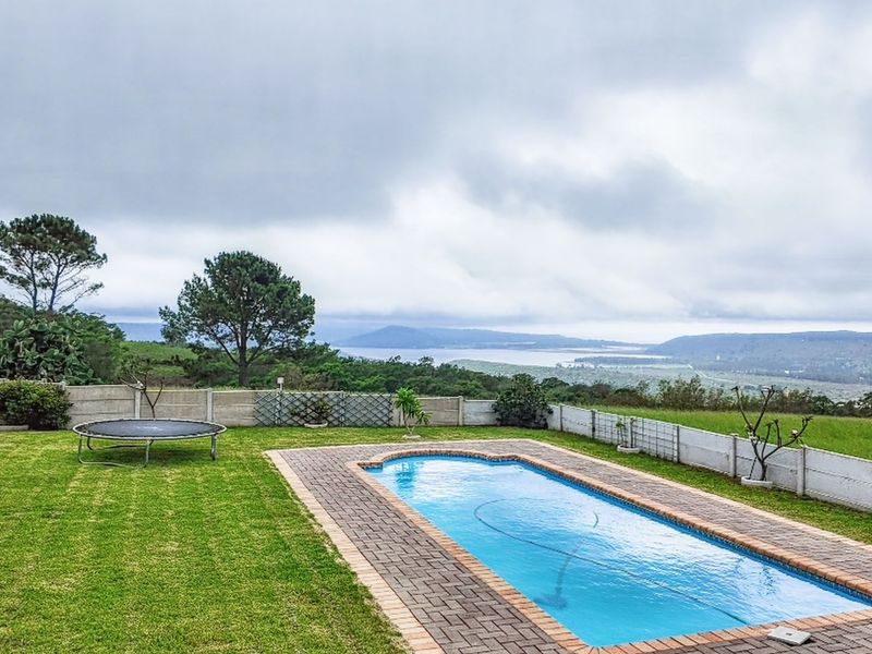 Outdoor pool area featuring a rectangular swimming pool with brick paving, set within a grassy garden overlooking a scenic landscape.