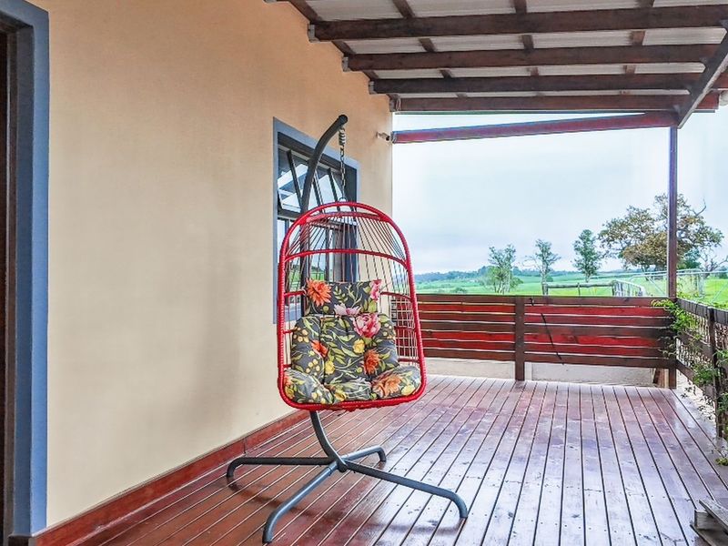 A covered timber deck patio featuring a wooden railing and direct access to the exterior, offering views of the surrounding farm landscape.