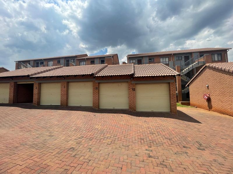 Exterior view of a residential apartment complex featuring a row of brick garages with roller shutter doors and a paved driveway.