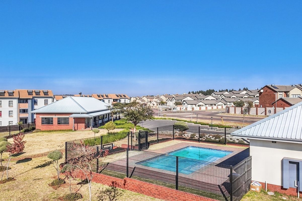 Aerial view of the apartment complex grounds, featuring a communal swimming pool, landscaped garden areas, and surrounding residential buildings.