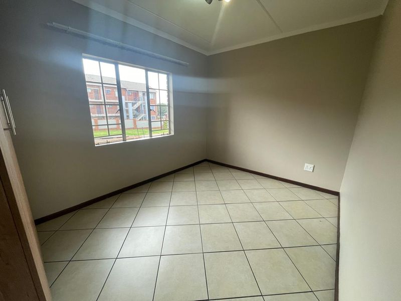 A clean, empty bedroom featuring neutral wall paint, tiled flooring, and a built-in cupboard, offering a blank canvas for personalization.