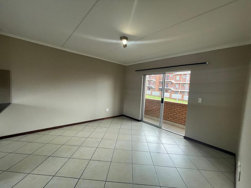 A bright, empty living room featuring neutral tiled flooring and a sliding glass door that opens onto a private balcony.