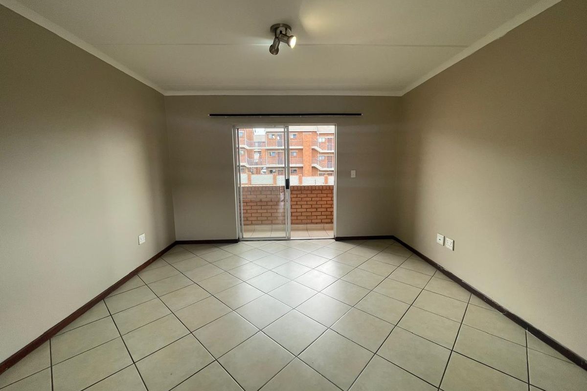 An empty, neutrally painted living room featuring tiled flooring and a sliding glass door that opens onto a balcony.