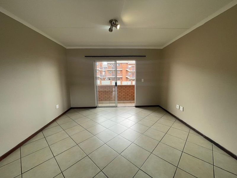 An empty, neutrally painted living room featuring tiled flooring and a sliding glass door that opens onto a balcony.