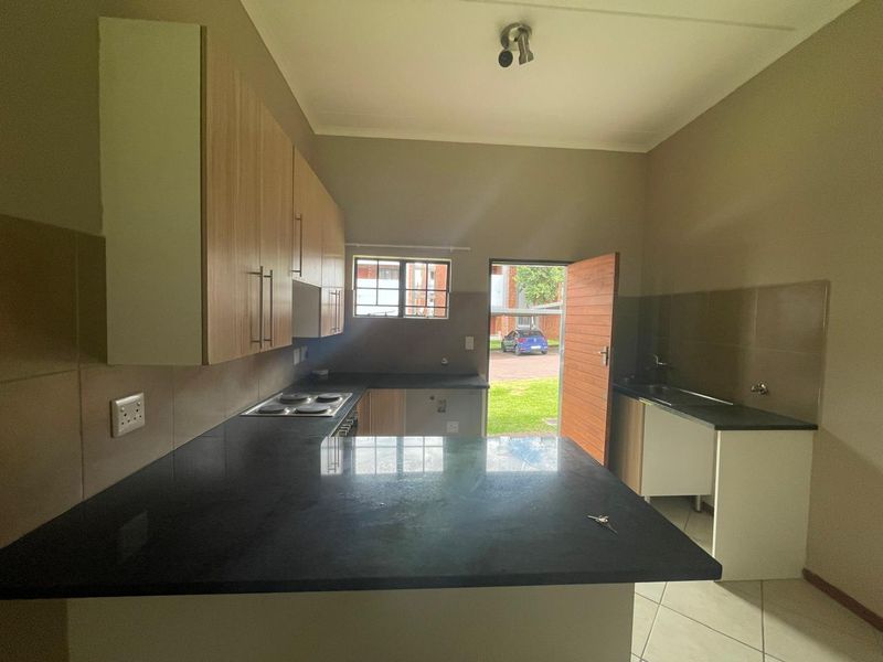 A functional kitchen featuring built-in cabinetry, stone countertops, an electric hob, and a double sink, with direct access to the exterior.
