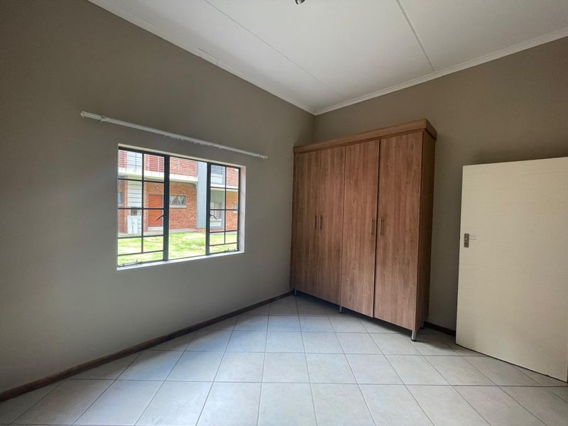 A bright, empty bedroom featuring neutral wall tones, tiled flooring, and a large built-in wooden wardrobe.