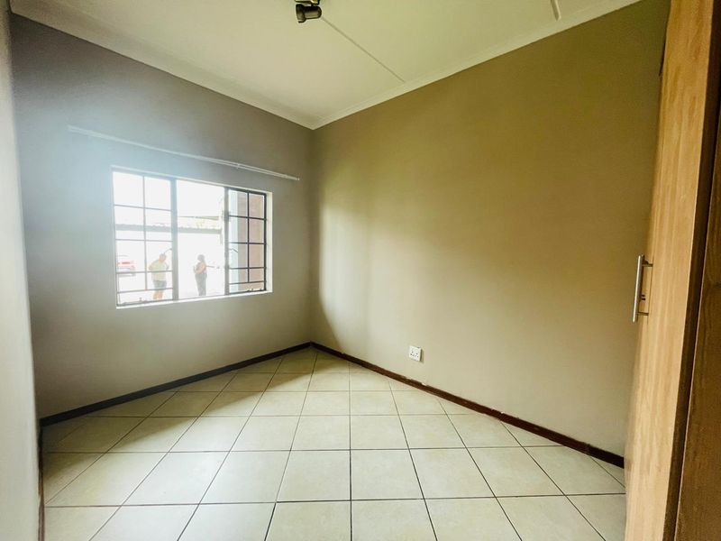 A clean, empty bedroom featuring neutral tiled flooring, a built-in cupboard, and a window with security bars.