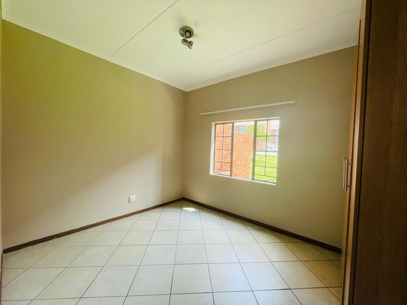 A clean, empty bedroom featuring neutral wall tones, tiled flooring, and a built-in cupboard, offering a versatile space ready for personalization.