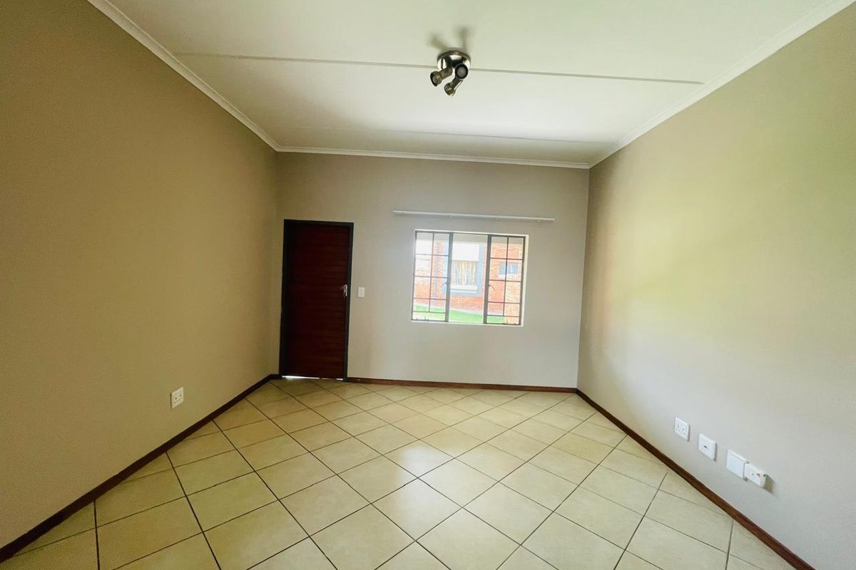 A clean, empty living room featuring neutral wall tones, tiled flooring, and a modern ceiling spotlight, providing a versatile space for personalization.