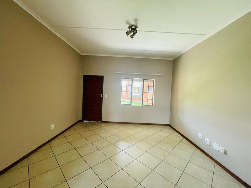 A clean, empty living room featuring neutral wall tones, tiled flooring, and a modern ceiling spotlight, providing a versatile space for personalization.