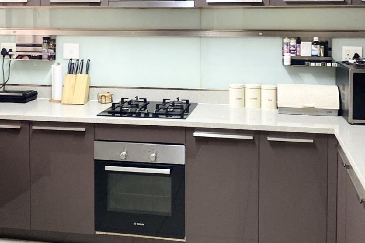 Modern kitchen featuring glossy cabinetry, stone countertops, a gas hob, built-in oven, and a sleek glass splashback with tiled flooring.