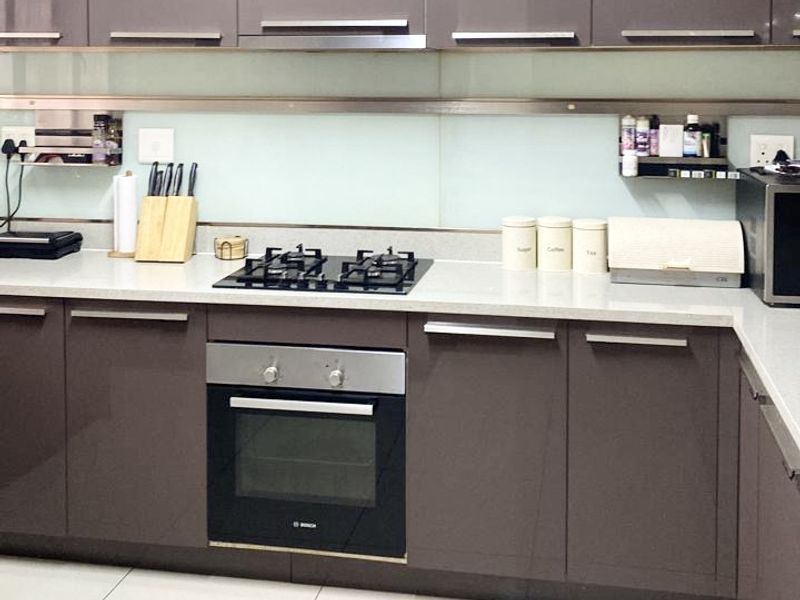 Modern kitchen featuring glossy cabinetry, stone countertops, a gas hob, built-in oven, and a sleek glass splashback with tiled flooring.