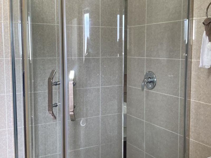 A bathroom featuring a curved glass shower enclosure with a rainfall shower head, complemented by neutral wall tiling and a modern vanity unit.